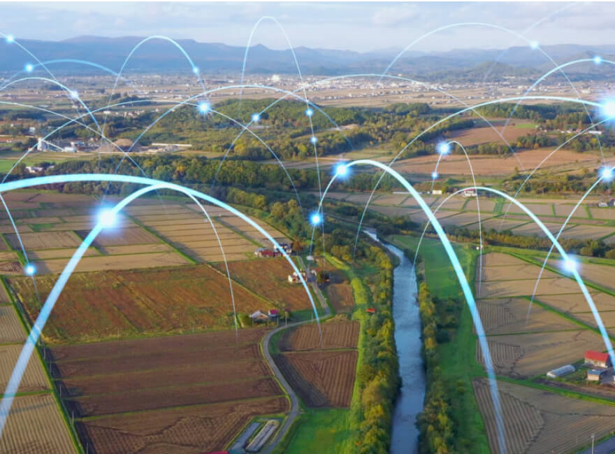 Bird's eye photo-realistic rendering of a futuristic scene depicting a vast range of agriculture fields with superimposed glowing archs representing automated drone and communitcation paths for work to be done. Although futuristic, the scene looks like something that could actually be taking place now.